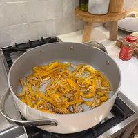Customer-uploaded image. Click to see more details. The image represents: A large white pan on a stovetop containing sautéed sliced onions and yellow bell peppers in a kitchen setting