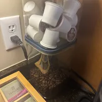 Customer-uploaded image. Click to see more details. The image represents: A clear storage container filled with white coffee cups and coffee pods sits on a kitchen counter next to coffee beans and tea packages