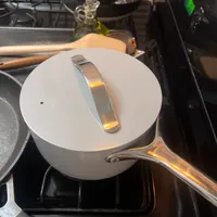 Customer-uploaded image. Click to see more details. The image represents: A white saucepan with lid and handle sitting on a stovetop burner in a kitchen