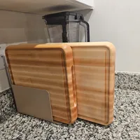 Customer-uploaded image. Click to see more details. The image represents: Three wooden cutting boards of different sizes leaning against a kitchen appliance on a granite countertop