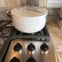 Customer-uploaded image. Click to see more details. The image represents: White ceramic pot with lid and handles sitting on a Wolf brand gas cooktop with stainless steel surface and black control knobs