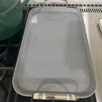 Customer-uploaded image. Click to see more details. The image represents: Glass baking dish with metal handles sitting on stovetop next to green pot