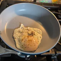 Customer-uploaded image. Click to see more details. The image represents: A chicken breast seasoned with black pepper cooking in a light-colored pot on a stovetop.