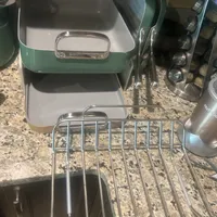 Customer-uploaded image. Click to see more details. The image represents: Kitchen counter with green and white ceramic baking dish, metal cooling rack, and stainless steel appliance on granite countertop