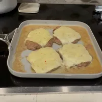 Customer-uploaded image. Click to see more details. The image represents: Four pieces of meat topped with melted cheese cooking in a white baking dish on a stovetop