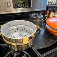 Customer-uploaded image. Click to see more details. The image represents: A stainless steel oven with digital display showing 4:39, stovetop with a gold-trimmed steamer basket, gray pot with lid, and orange cookware visible on the cooktop surface.