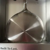 Customer-uploaded image. Click to see more details. The image represents: Stainless steel saute pan with lid stored in kitchen cabinet, with product marketing text highlighting durability and eco-friendly features