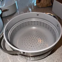 Customer-uploaded image. Click to see more details. The image represents: A stainless steel steamer basket with perforated holes sitting on a kitchen counter next to other cookware