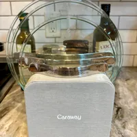 Customer-uploaded image. Click to see more details. The image represents: A white Caraway brand kitchen container with glass lid sits on a countertop with subway tile backsplash, wine bottles visible in the background.