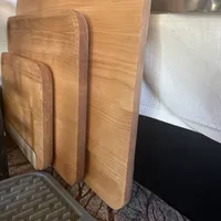 Customer-uploaded image. Click to see more details. The image represents: Several wooden cutting boards of different sizes leaning against a kitchen counter, with a plastic dish drying rack visible in the foreground