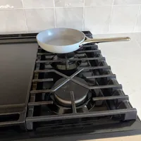 Customer-uploaded image. Click to see more details. The image represents: A white ceramic frying pan with a metal handle sits on a gas stovetop burner in a kitchen with white subway tile backsplash.