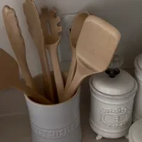 Customer-uploaded image. Click to see more details. The image represents: A white ceramic utensil holder containing wooden kitchen utensils including spoons, spatulas, and a whisk, displayed next to white ceramic canisters on a countertop.