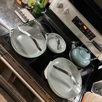 Customer-uploaded image. Click to see more details. The image represents: A stovetop with glass cookware and lids arranged on the burners, alongside a blue teapot and various condiment bottles and kitchen items on the counter above.