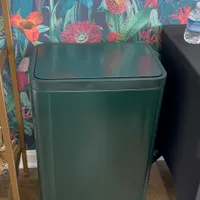 Customer-uploaded image. Click to see more details. The image represents: A green rectangular trash can with a foot pedal at the base, positioned in front of a dark wallpaper featuring colorful botanical illustrations with red and pink flowers, green leaves, and blue accents.