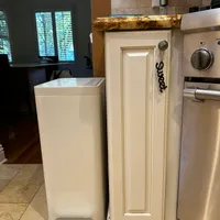 Customer-uploaded image. Click to see more details. The image represents: Kitchen interior showing white cabinets with granite countertops, stainless steel appliances including a dishwasher, and a white step-on trash can on tile flooring