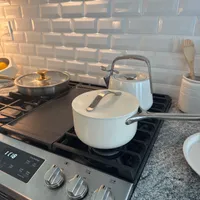 Customer-uploaded image. Click to see more details. The image represents: A modern kitchen stovetop with white cookware including a pot and kettle, set against a white subway tile backsplash. The stove has stainless steel controls and black burner grates. A granite countertop is visible to the right with kitchen utensils in a container.