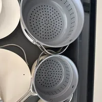 Customer-uploaded image. Click to see more details. The image represents: Two white colanders with perforated holes stacked in a kitchen drawer among other cookware