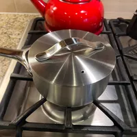 Customer-uploaded image. Click to see more details. The image represents: Stainless steel saucepan with lid on gas stovetop with red kettle in background