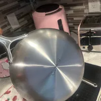Customer-uploaded image. Click to see more details. The image represents: A stainless steel frying pan with a brushed metal finish sits on a kitchen counter next to a stovetop, with a colorful strawberry-patterned kitchen towel underneath
