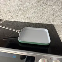 Customer-uploaded image. Click to see more details. The image represents: A white and mint green rectangular baking pan sits on a black electric cooktop with a digital display showing 5:59 and control knobs on the right side.