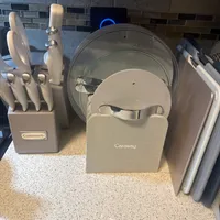 Customer-uploaded image. Click to see more details. The image represents: Kitchen counter with organized cookware including a Cuisinart knife block, Caraway pot lids in a fabric holder, and utensils against a tile backsplash