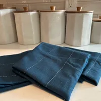 Customer-uploaded image. Click to see more details. The image represents: Navy blue kitchen towels with white stitching folded on a white countertop, with ceramic storage canisters with wooden lids in the background