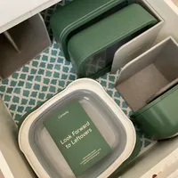 Customer-uploaded image. Click to see more details. The image represents: A drawer organizer containing green and white food storage containers with lids, arranged on a patterned teal and white fabric liner. One container displays text reading "Look Forward to Leftovers" with the Caraway brand logo visible.