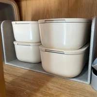Customer-uploaded image. Click to see more details. The image represents: Four cream-colored storage containers with lids arranged on a gray fabric organizer mat inside a wooden cabinet or shelf.