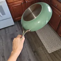 Customer-uploaded image. Click to see more details. The image represents: A person holding a mint green ceramic bowl with a stainless steel interior and metal handle in a kitchen with dark wood cabinets and gray flooring.