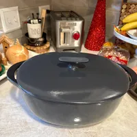 Customer-uploaded image. Click to see more details. The image represents: A large black cooking pot with lid sits on a kitchen counter surrounded by various kitchen items including a toaster, utensil holder, and fruit bowl