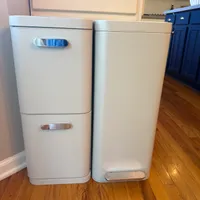 Customer-uploaded image. Click to see more details. The image represents: Two stainless steel kitchen trash cans with step-open lids sitting on hardwood floor in a kitchen