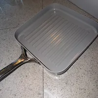 Customer-uploaded image. Click to see more details. The image represents: A square stainless steel grill pan with ridged bottom sitting on a speckled granite countertop