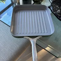 Customer-uploaded image. Click to see more details. The image represents: A square grill pan with ridged bottom sitting on a glass stovetop surface