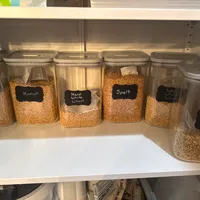 Customer-uploaded image. Click to see more details. The image represents: Organized pantry shelf with clear storage containers holding various grains and cereals, each labeled with black chalkboard-style tags including Einkorn, Kamut, Hard White Wheat, Spelt, Soft White Wheat, and Oat Groats