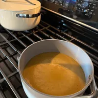 Customer-uploaded image. Click to see more details. The image represents: A large pot of golden broth or soup simmering on a stovetop with another covered pot in the background