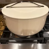 Customer-uploaded image. Click to see more details. The image represents: White ceramic Dutch oven with lid and handles sitting on a gas stove burner