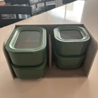 Customer-uploaded image. Click to see more details. The image represents: Two stacked green food storage containers with translucent lids, held in a beige fabric organizer on a kitchen table.