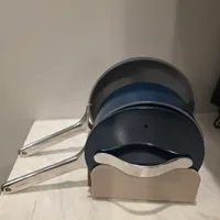 Customer-uploaded image. Click to see more details. The image represents: A set of three nesting saucepans with stainless steel handles in varying sizes, displayed on a beige Caraway brand stand. The pans feature a dark navy blue exterior with a light blue interior band, arranged from smallest to largest.