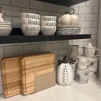 Customer-uploaded image. Click to see more details. The image represents: Kitchen shelves displaying white bowls labeled "NOURISH", wooden cutting boards, white plates, a decorative pumpkin, and various kitchen accessories against white subway tile backsplash