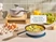 Caraway navy mini skillet cooking eggs beside a lidded mini sauce pan on a wooden organizer.