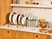 Caraway white cookware and glass lids with gold-tone handles arranged in countertop organizers.