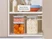 Caraway glass airtight containers stacked with dry ingredients in a cabinet beside colorful lids.