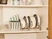 Caraway glass lids and Cream cookware stored upright in organizers inside a cabinet.