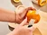 Hands using a paring knife to peel an orange over a cutting board.