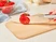 Hand slicing a tomato with a gray-handled kitchen knife on a wooden cutting board.